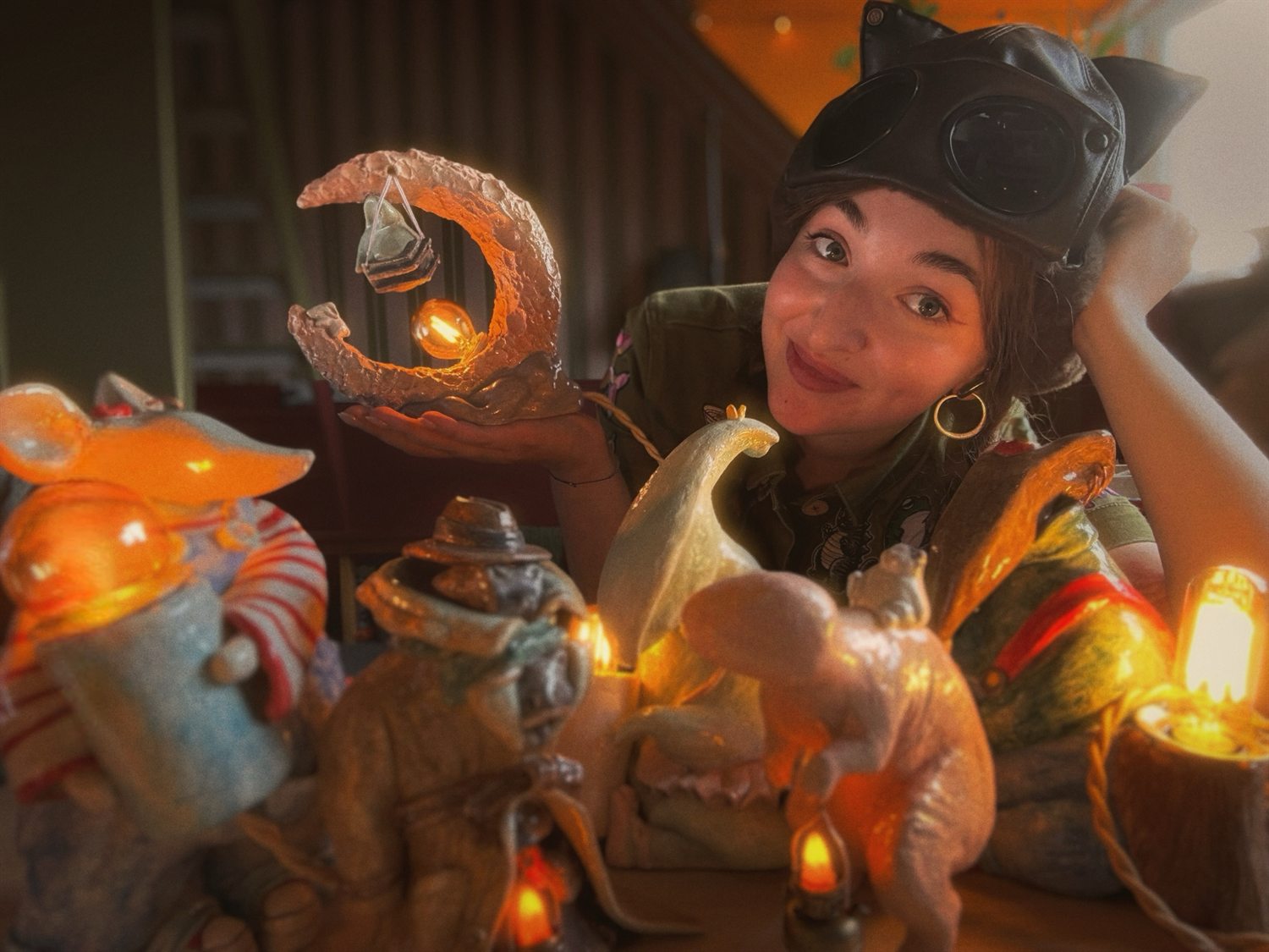 Alisa surrounded by her glowing ceramic creature lamps, holding up a moon-shaped nightlight